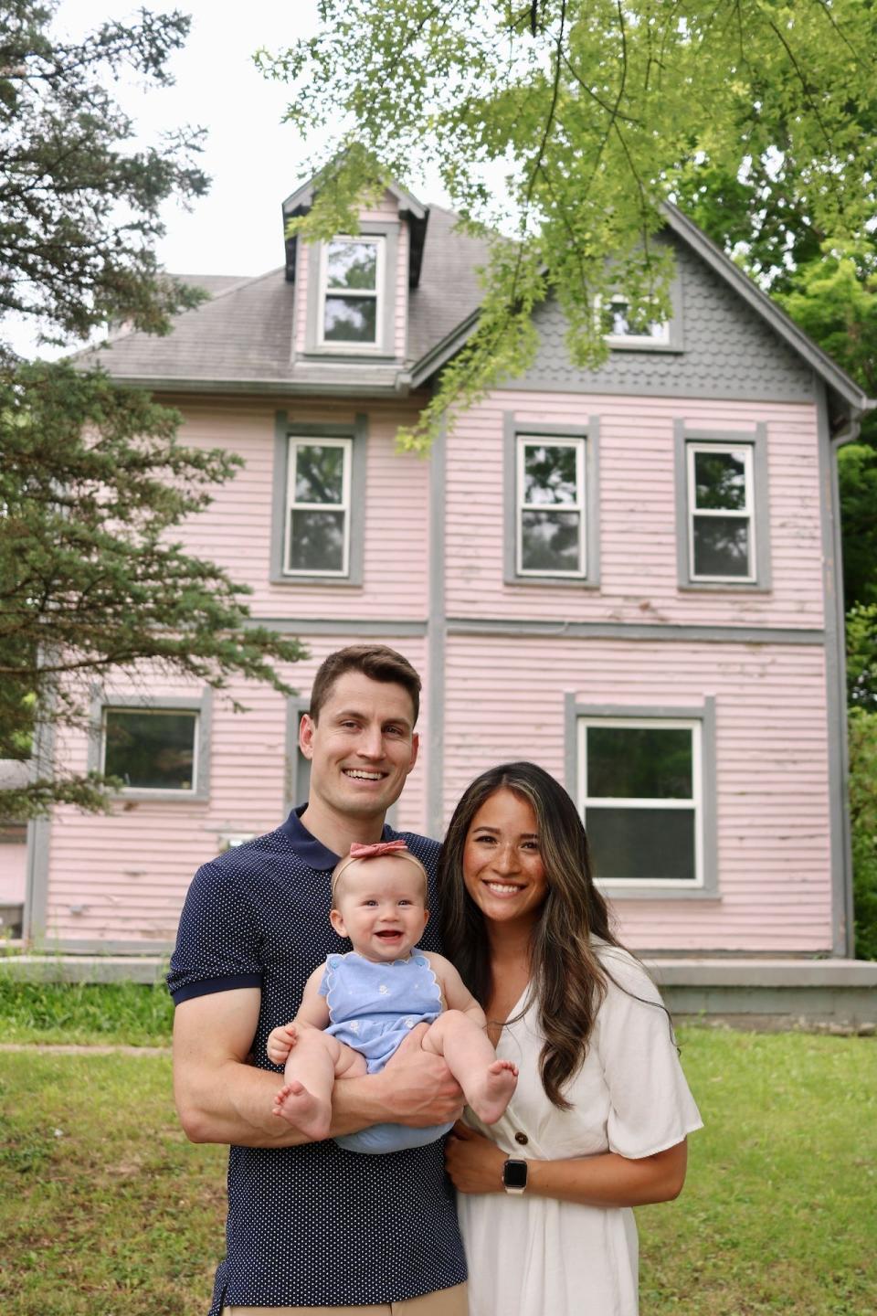 Becky and Drew Bidlen carrying their daughter in front of their new home.