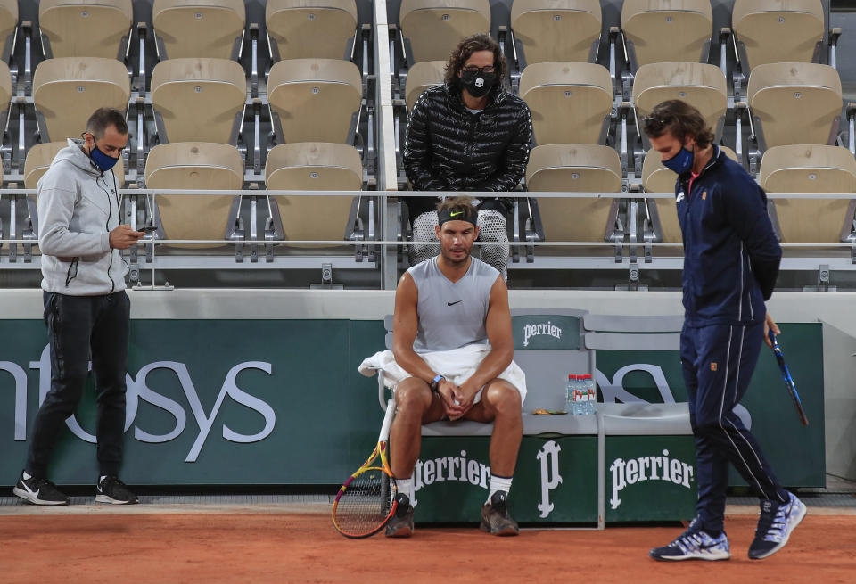 Spain's Rafael Nadal, center, coach Francisco Roig, right, and his staff wearing face masks to prevent the spread of coronavirus gather during a break at the Roland Garros stadium during practicing in Paris, Friday, Sept. 25, 2020. Already repeatedly trimmed, crowd sizes for the French Open have been reduced again to just 1,000 spectators per day because of the worsening coronavirus epidemic in Paris. (AP Photo/Michel Euler)