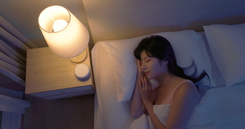 Woman sleeping peacefully beside a glowing bedside lamp