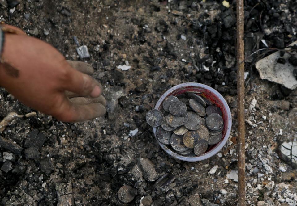 In this Thursday, Jan. 26, 2017 photo, Claudia Salinas salvages charred coins, which belong to her daughter, as she culls through the remains of their home destroyed by wildfires in Santa Olga, Chile. The flames engulfed the post office, a kindergarten, and about 1,000 homes in the town, located south of the Chilean capital. (AP Photo/Esteban Felix)
