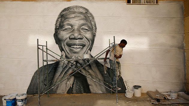 Nelson Tavares, 24, originally from Cape Verde, works on a graffiti of Nelson Mandela which he painted during festivities in his neighbourhood. Photo: Getty.