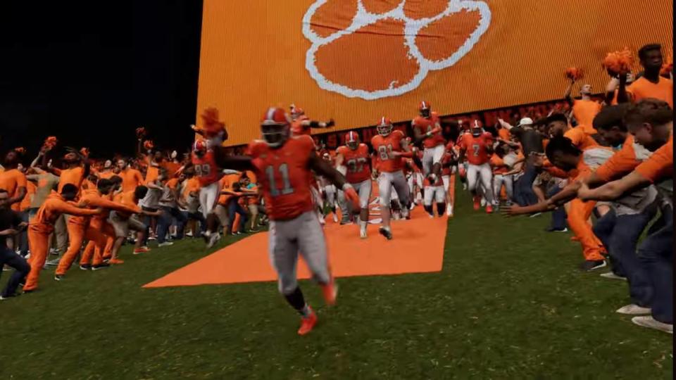Surrounded by student fans, virtual Clemson football players run down The Hill in the east end zone of Memorial Stadium for a night game in EA Sports College Football 25. Behind them is Clemson’s video board, which was updated in 2022 and is one of the largest in the country.