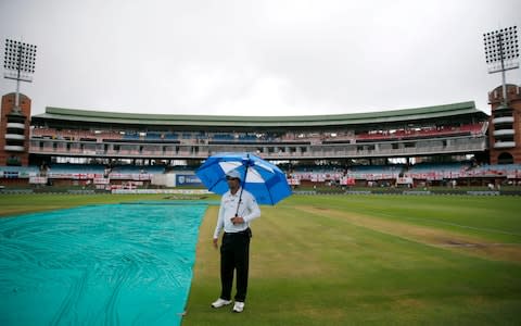 A match official stands under an umbrella next to the cover covering the pitch before the start of the match on the second day of the third Test cricket match between South Africa and England at the St George's Park Cricket Ground - Credit: GETTY IMAGES