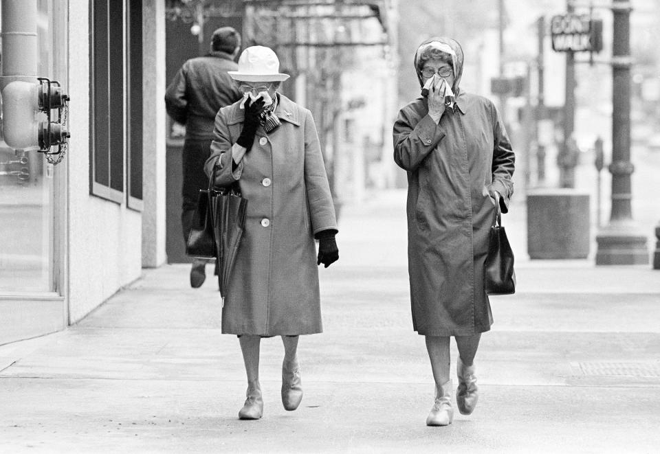 Two women cover up as they walk along a Portland street, May 26, 1980, after Mount St. Helens erupted spewing ash skyward with some of it landing on the city. Work crews have already started washing off the streets.
