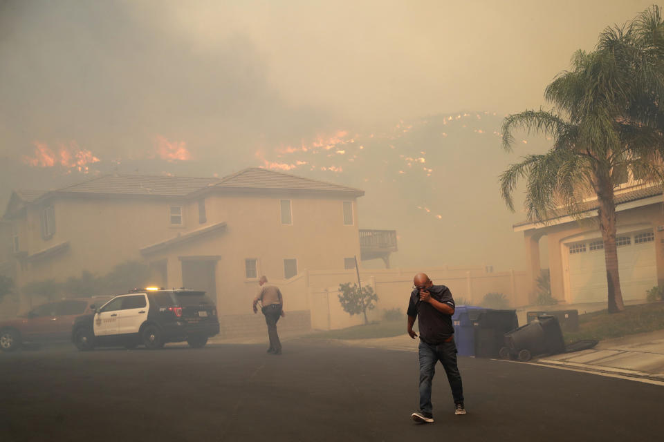 A resident covers his face as he is evacuated as a wildfire approaches Thursday, Oct. 24, 2019, in Santa Clarita, Calif. (AP Photo/Marcio Jose Sanchez)
