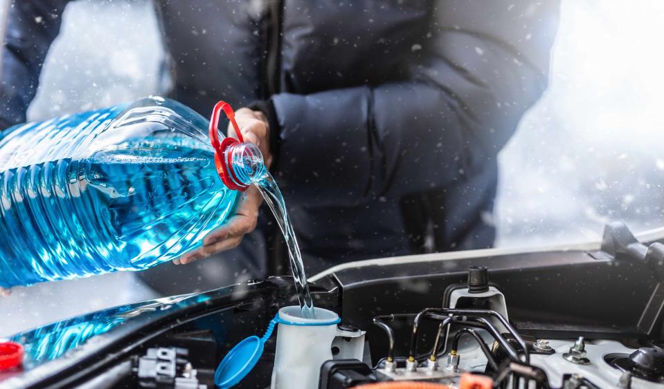 A man pours windshield wiper spray into the car during a snowstorm.