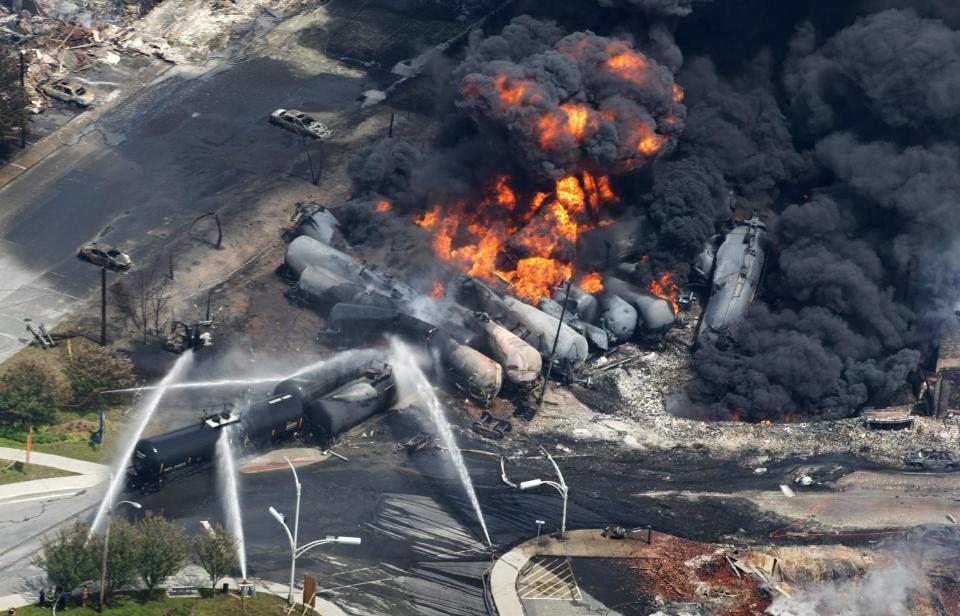 FILE - In a , Saturday, July 6, 2013 file photo, smoke rises from railway cars that were carrying crude oil after derailing in downtown Lac Megantic, Quebec, Canada. Railroads that haul volatile crude shipments have reached an agreement with U.S. transportation officials to adopt wide-ranging voluntary safety measures after a string of explosive and deadly accidents. A copy of the agreement between the U.S. Transportation Department and the Association of American Railroads obtained Friday, Feb. 21, 2014 by The Associated Press calls for railroads to slow down oil trains through major cities, increase track inspections and bolster emergency response planning along routes that see trains that can haul up to three million gallons of oil each. (AP Photo/The Canadian Press, Paul Chiasson, File)