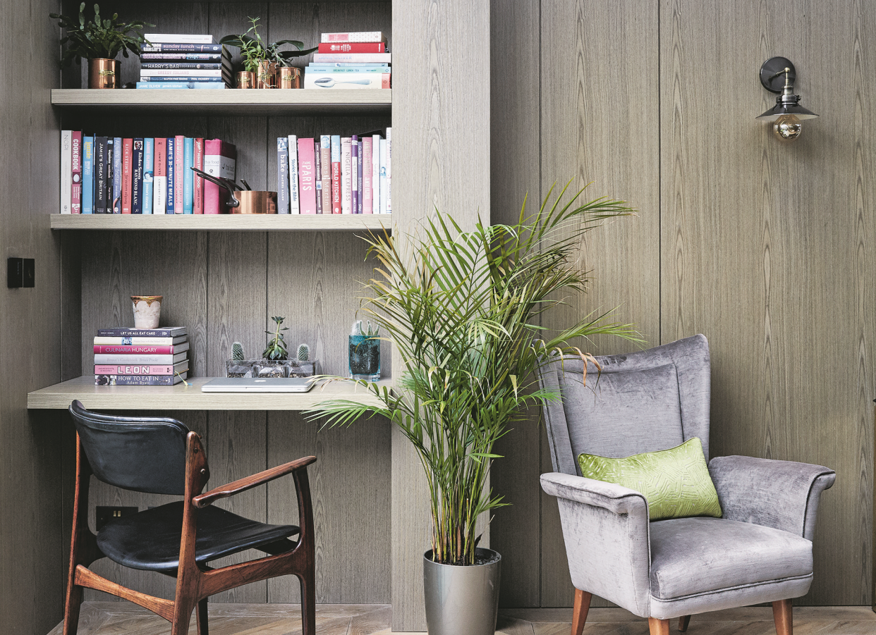  A home office with book shelves, an arm chair, and a fern. 