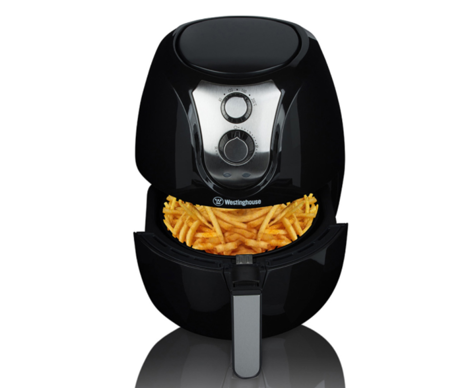 A black Westinghouse air fryer sits on a white background with its tray open revealing hot chips.
