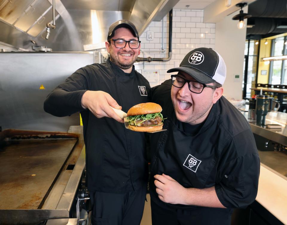 Brockton Beer Company co-head chefs from left, Christos Liapopoulos and Markos Liapopoulos with a BBC Burger topped with BBC bourbon bacon jam, brie cheese, pickles and arugula on Wednesday, May 1, 2024.