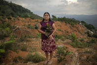 Olga Ondina, 52, stands for a portrait at the site of her home which was destroyed by a landslide triggered by hurricanes Eta and Iota in the village of La Reina, Honduras, Wednesday, June 23, 2021. "I love flowers, and now I take a bouquet with me where I now live in a rented house. Everything that happened to us is very sad, my parents lived and died here, my children were born here. Today I came to cry," she said. (AP Photo/Rodrigo Abd)