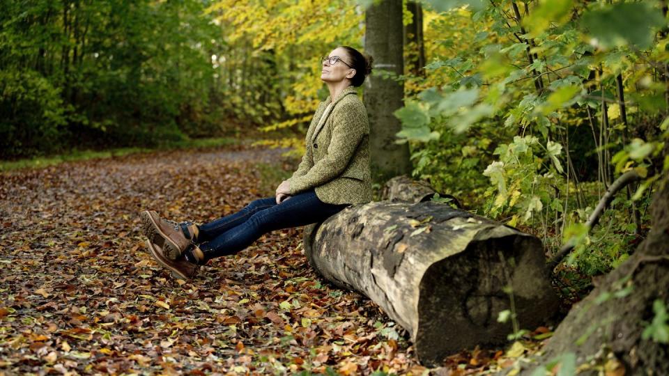mature woman sitting on a tree trunk in a autumn forest