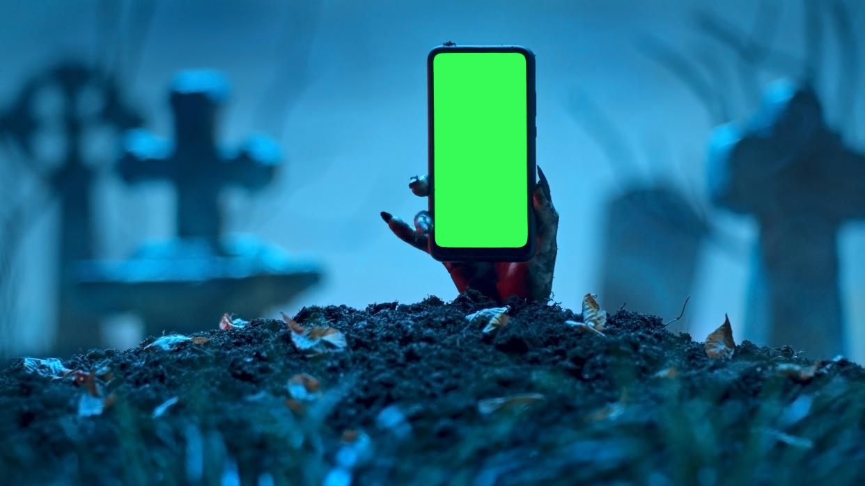  A smartphone held in a zombie had, emerging from a spooky crypt. 