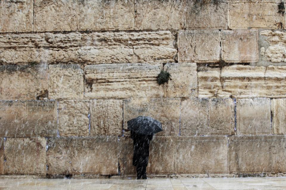 A man holding an umbrella prays at the Western Wall in Jerusalem's Old City during a snowstorm in winter