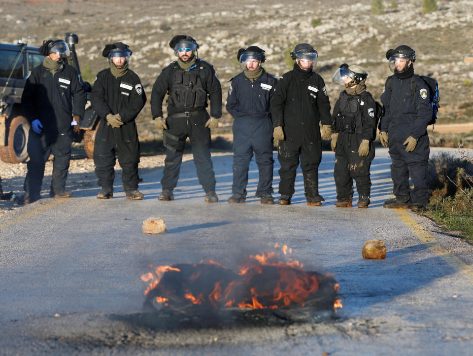 Israeli policemen stand next to a burning tyre on a road near the entrance to the Israeli settler outpost of Amona.