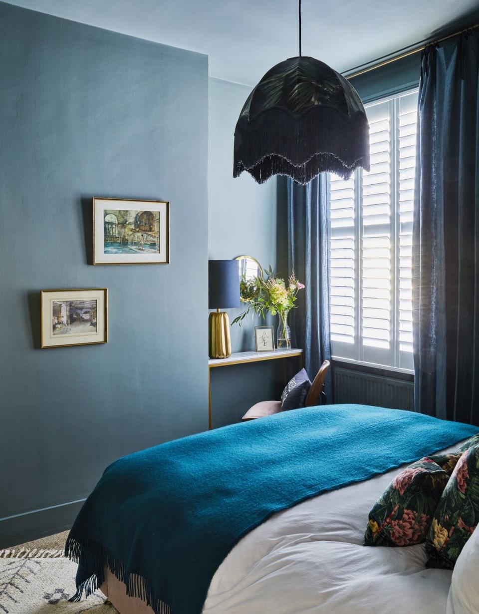 a room with a blue bed throw, walls and fringed pendant