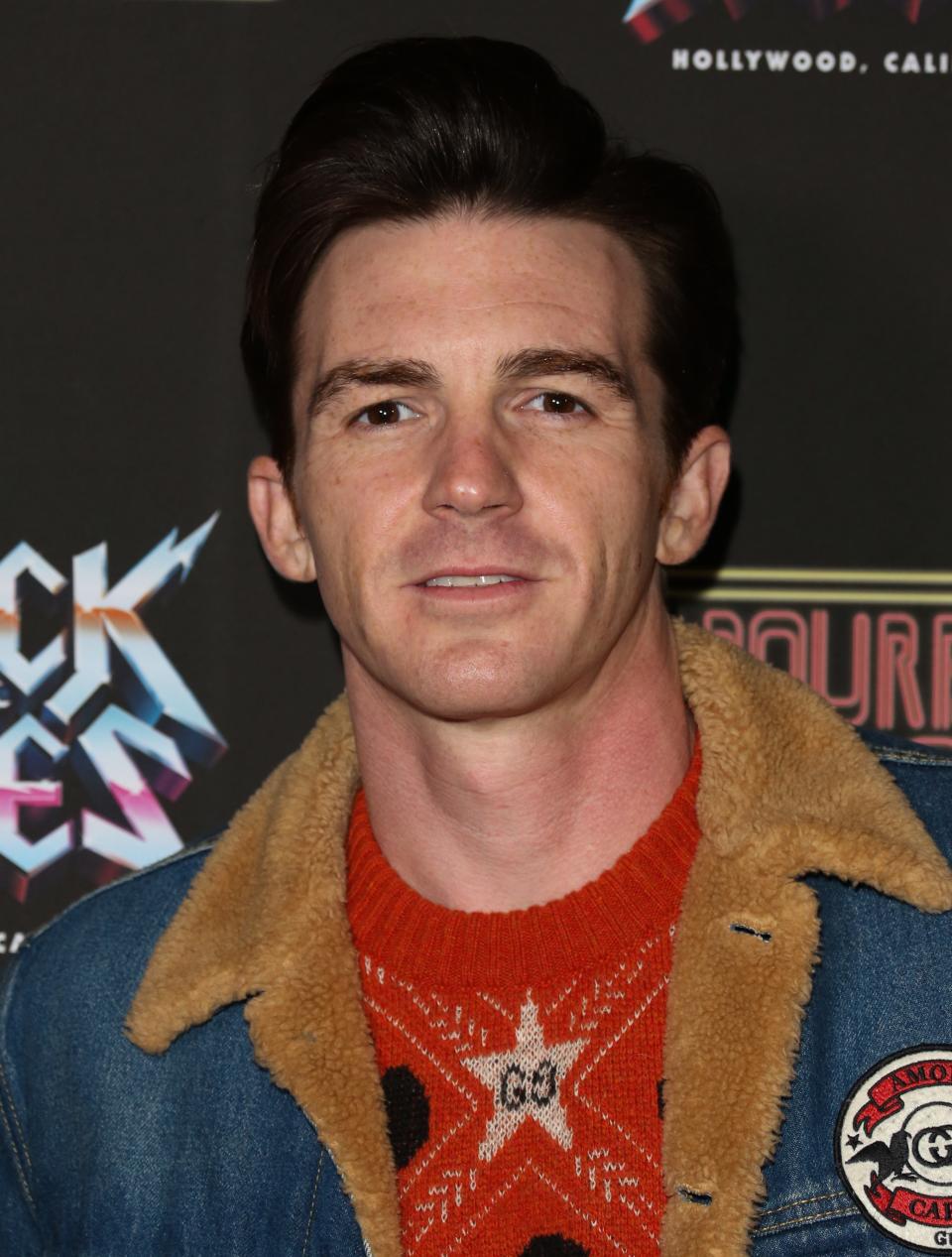 Drake Bell in a denim jacket over a star-patterned shirt, smiling at a "Rock the Vote" event