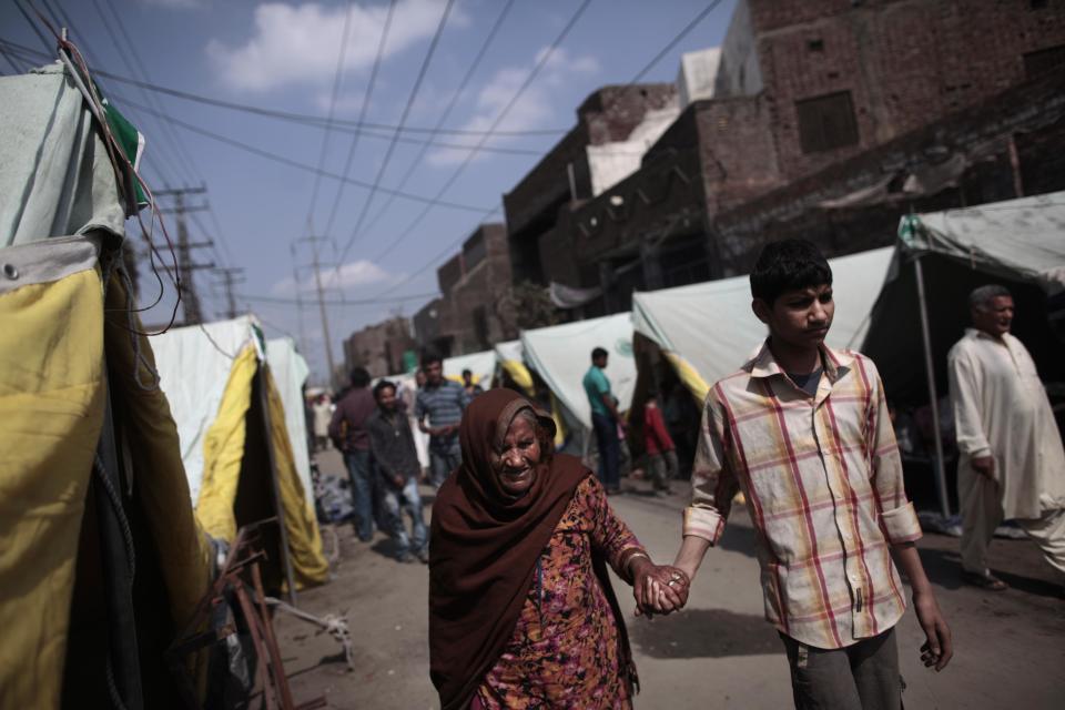 In this Thursday, March 13, 2014 photo, Pakistani Christians walk by tents where they took shelter after their homes were damaged by an angry Muslim mob in a Christian neighborhood, in Lahore, Pakistan. Pakistan’s blasphemy law has become a potent weapon in the arsenal of Muslim extremists, who use it against adherents of minority religions. (AP Photo/Nathalie Bardou)