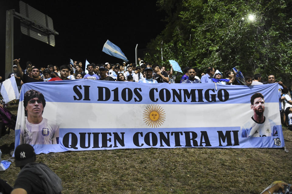 BUENOS AIRES, ARGENTINA - DECEMBER 20: Fans of Argentina display a flag of Lionel Messi and late football legend Diego Maradona before the arrival of the Argentina men's national football team after winning the FIFA World Cup Qatar 2022 on December 20, 2022 in Buenos Aires, Argentina. (Photo by Rodrigo Valle/Getty Images)