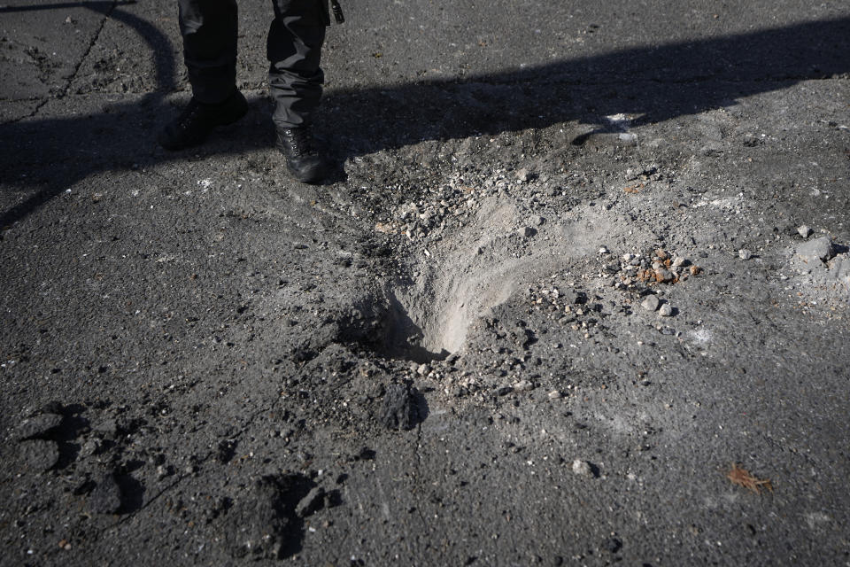 An Israeli police officer stands beside a crater where remains of an intercepted rocket fired from Lebanon fell in Shlomi, northern Israel Thursday, April 6, 2023. Israeli air defenses intercepted a rocket fired from Lebanon into northern Israel, the Israeli military said. It was not immediately clear who was behind the rare rocket fire from Lebanon. (AP Photo/Ariel Schalit)