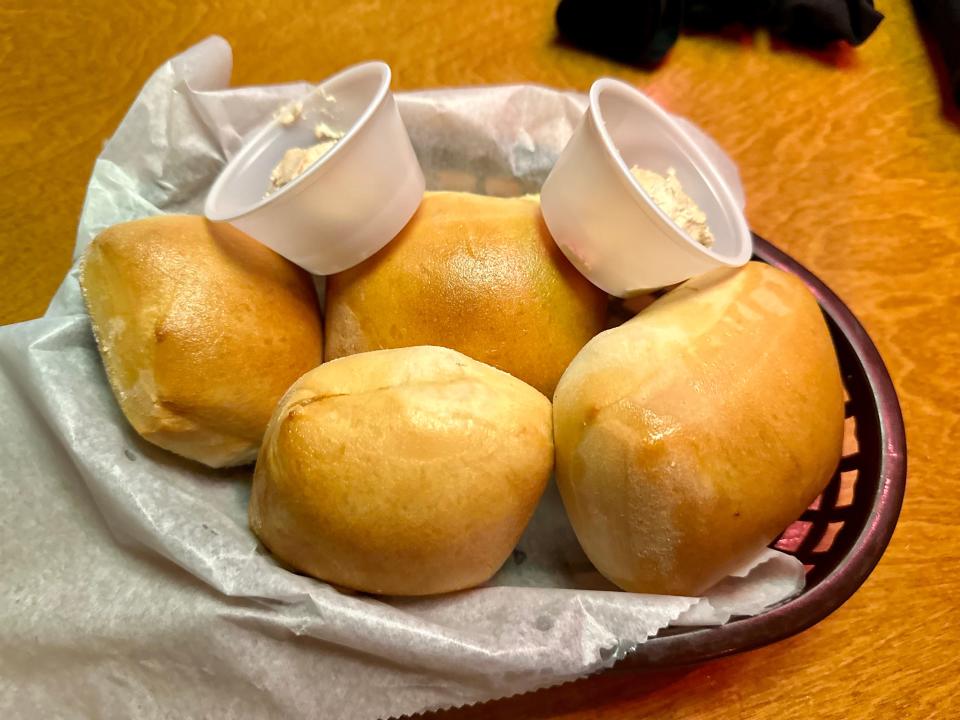 Basket of Texas Roadhouse rolls with two small cups of cinnamon butter