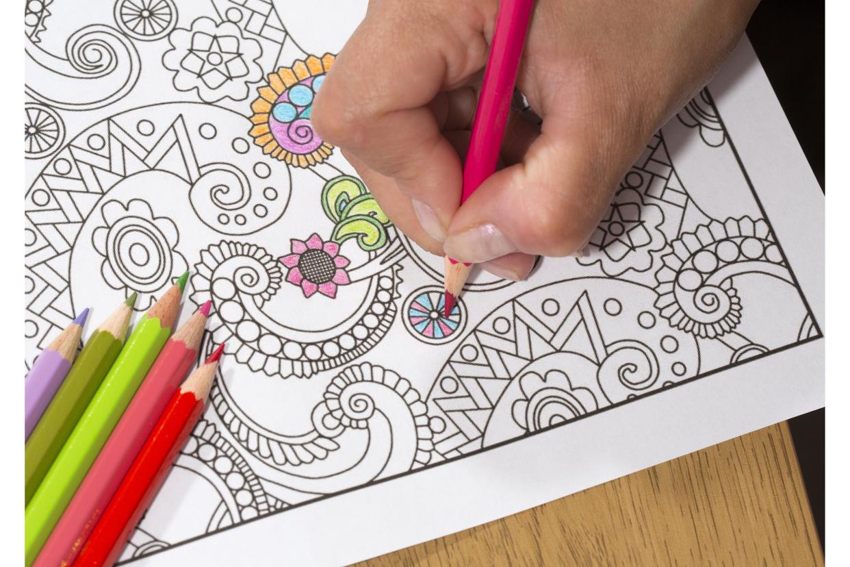 Closeup of hand coloring in an adult coloring book with colored pencils