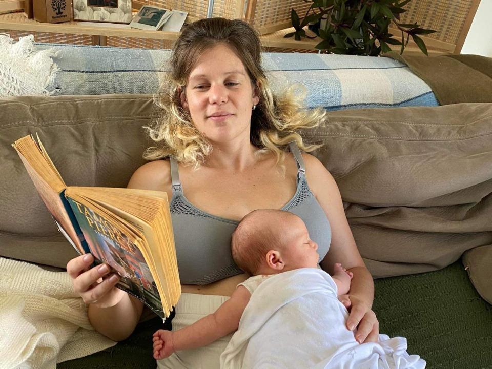 Mother reading a book on coach with baby laying on her.