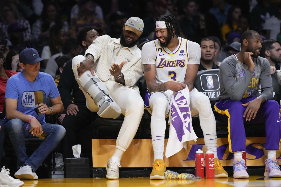 Los Angeles Lakers' LeBron James, center left, shows his orthopedic boot to Anthony Davis on the bench during the first half of an NBA basketball game against the Golden State Warriors, Sunday, March 5, 2023, in Los Angeles. (AP Photo/Jae C. Hong)
