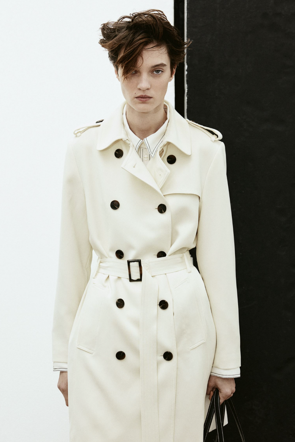 woman wearing white trench coat with black buttons, Double-Breasted Trenchcoat (Photo via H&M)