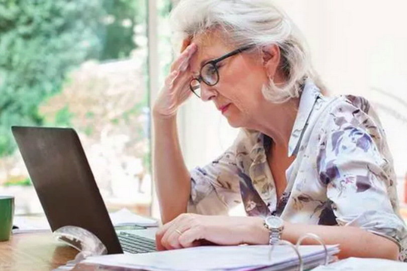 An elderly woman is looking at paperwork with a worried expression on her face