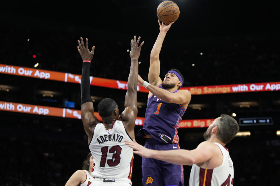 Phoenix Suns guard Devin Booker (1) looks to shoot over Miami Heat center Bam Adebayo (13) and forward Kevin Love, right, during the first half of an NBA basketball game, Friday, Jan. 5, 2024, in Phoenix. (AP Photo/Rick Scuteri)