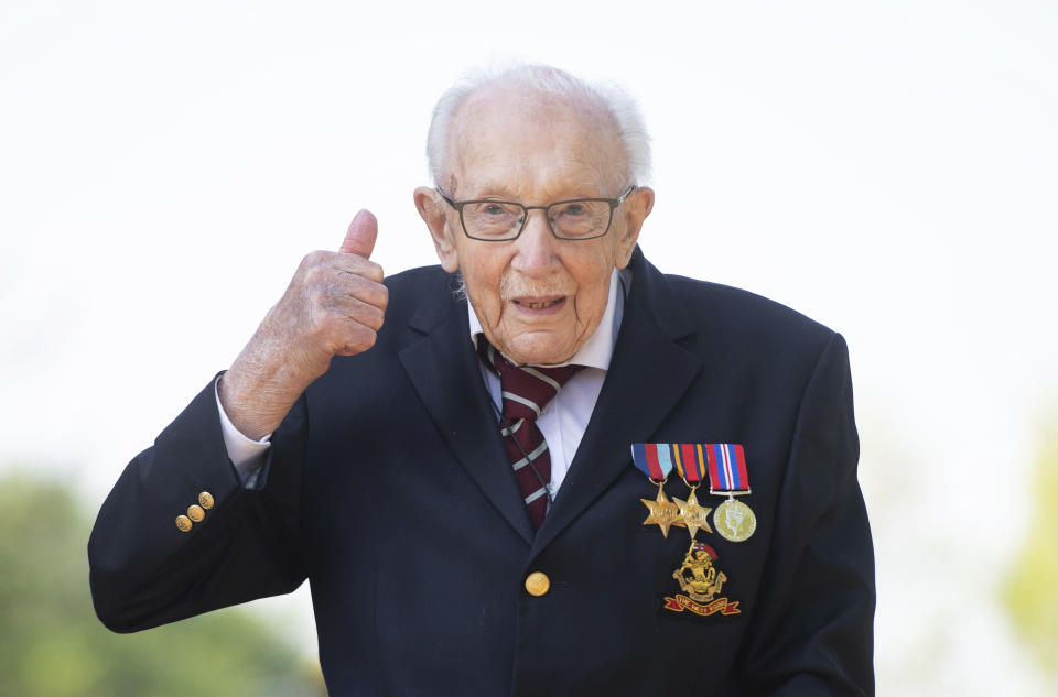 FILE - In this April 16, 2020, file photo, Captain Tom Moore gestures at his home in Marston Moretaine, Bedfordshire, England. The British army veteran who shuffled the length of his garden 100 times to raise funds for the National Health Service is to be honored with a knighthood. Moore received a special nomination for the honor from Prime Minister Boris Johnson, announced on Tuesday, May 19, just weeks after he raised 33 million pounds ($40 million) for completing a challenge to mark his 100th birthday. (Joe Giddens/PA via AP, File)