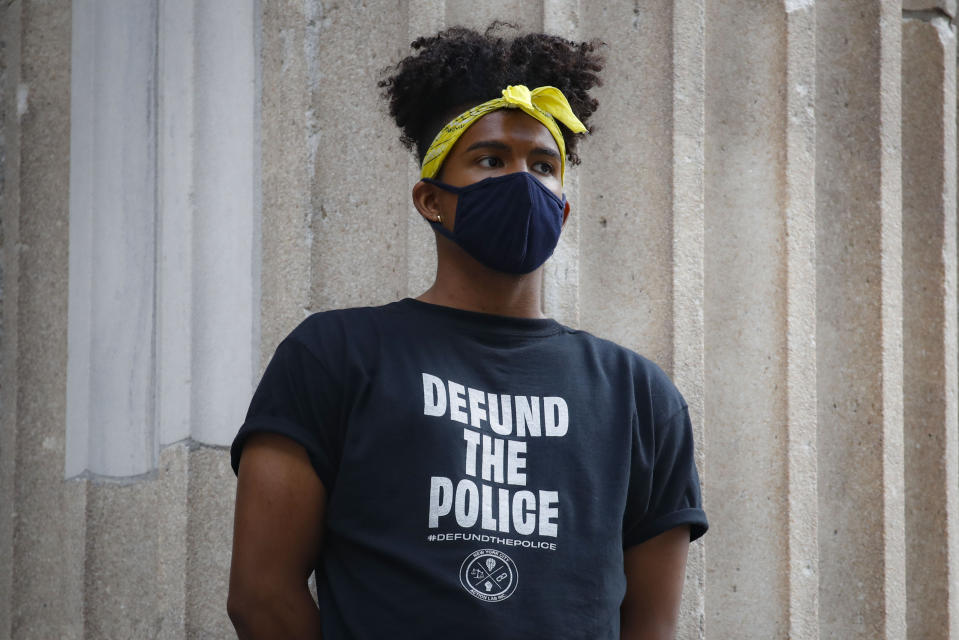A protester stands on the steps of a government building near an encampment outside City Hall, Tuesday, June 30, 2020, in New York. City Council members were due to debate and vote Tuesday night on a plan to shift $1 billion from policing to education and social services, with time running short ahead of the fiscal year that begins Wednesday. (AP Photo/John Minchillo)