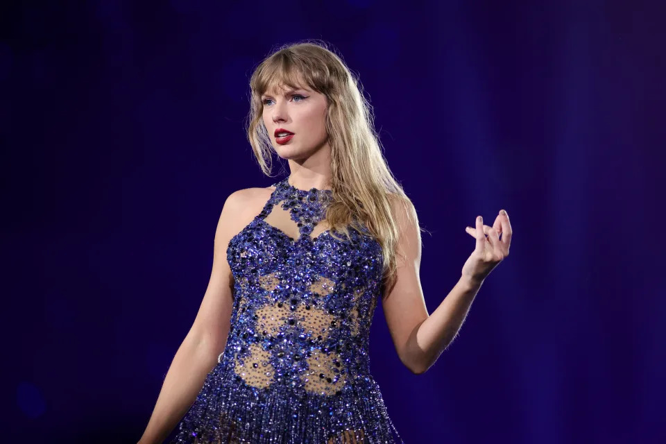 Taylor Swift performs on stage wearing a sleeveless, embellished gown with a beaded pattern