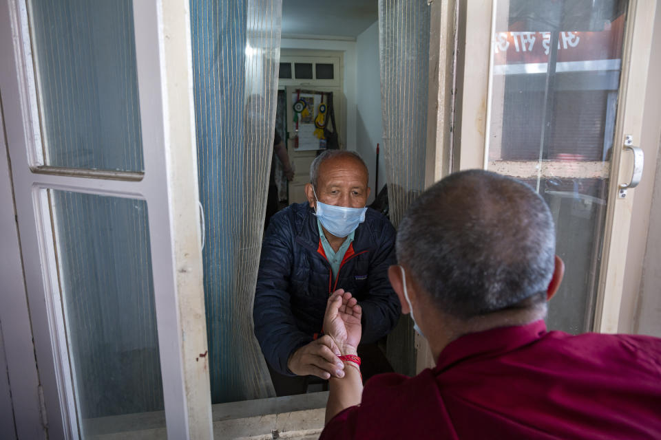 An exile Tibetan doctor practicing traditional medicine checks the pulse of a Tibetan Buddhist monk through the window of a clinic in Dharmsala, India, Thursday, April 16, 2020. Indian Prime Minister Narendra Modi on Tuesday extended the world's largest coronavirus lockdown to head off the epidemic's peak, with officials racing to make up for lost time. (AP Photo/Ashwini Bhatia)