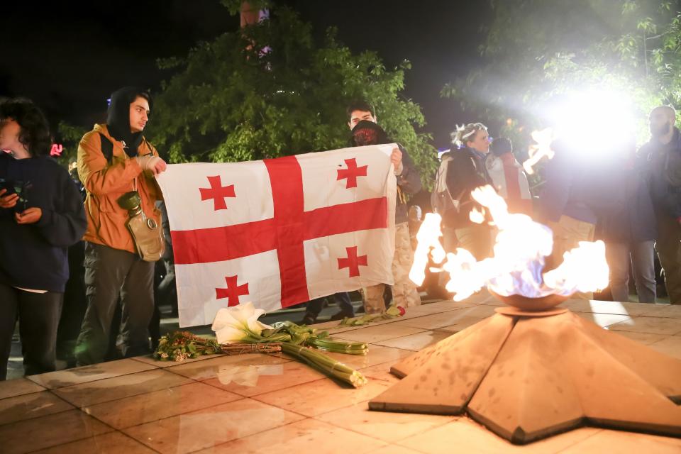 Demonstrators hold a Georgian national flag in front of an Eternal flame at the Square of Heroes during an opposition protest against "the Russian law" in the center of Tbilisi, Georgia, Tuesday, May 14, 2024. The Georgian parliament on Tuesday approved in the third and final reading a divisive bill that sparked weeks of mass protests, with critics seeing it as a threat to democratic freedoms and the country's aspirations to join the European Union. (AP Photo/Zurab Tsertsvadze)