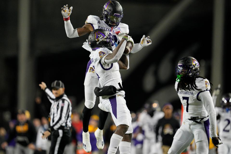 East Carolina safety Jireh Wilson, center, celebrates with teammate Julius Wood after making an interception during the first half of an NCAA college football game against Cincinnati, Friday, Nov. 11, 2022, in Cincinnati. (AP Photo/Jeff Dean)