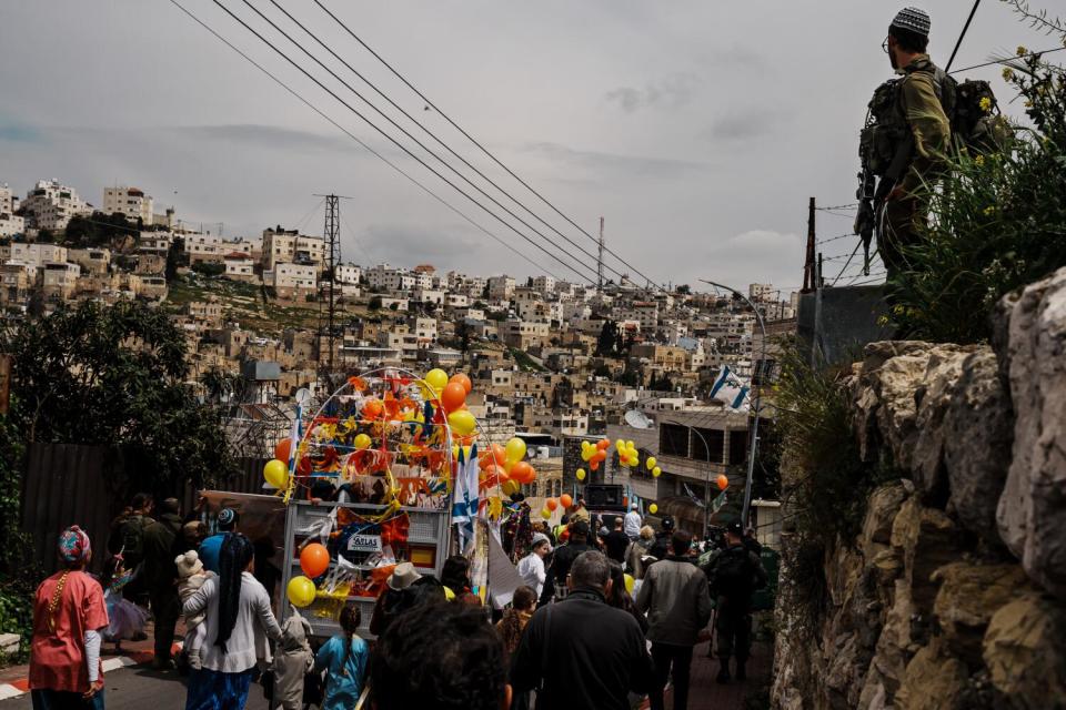 An Israeli soldier stands guard over Jewish settlers attending a parade in the West Bank Town the Hebron.