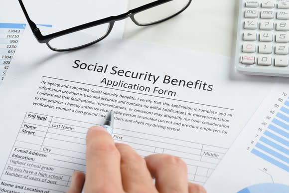 a pair of glasses on a social security benefits application form and a hand holding a pen next to it, too