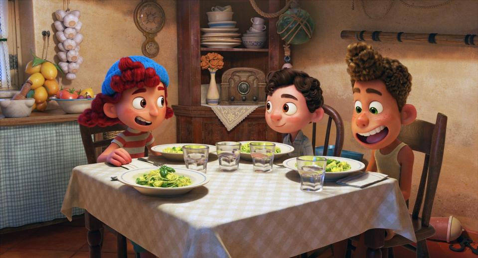 Animated characters Luca, Alberto, and Giulia from the movie "Luca" sit around a table enjoying a pasta meal and chatting inside a cozy kitchen