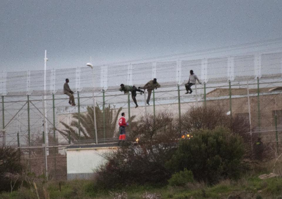 Sub-Saharan migrants climb over a metallic fence that divides Morocco and the Spanish enclave of Melilla, as a Red Cross worker is on-hand to offer humanitarian assistance, Monday Feb. 17, 2014. A Spanish official says about 200 sub-Saharan migrants stormed a barbed-wire border fence along Spain's northwest African enclave of Melilla, with about 50 of them making it over. A spokesman for the Interior Ministry's office in Melilla said the melee began early Monday. The Spanish city of Melilla lies on the African continent, surrounded by Morocco and the Mediterranean Sea. Migrants hoping to get to Europe camp on the Moroccan side, with several thousand trying each year to enter the city and Spain's other coastal enclave of Ceuta. (AP Photo/ Jesus Blasco de Avellaneda)