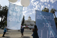 FILE-- In this Aug. 28, 2019, photo, supporters of a measure to limit when companies can label workers as independent contractors display banners in support of the bill during a rally at the Capitol in Sacramento, Calif. California lawmakers are debating a bill that would make companies like Uber and Lyft label their workers as employees, entitling them to minimum wage and benefits. (AP Photo/Rich Pedroncelli, File)