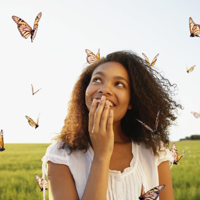  A woman holds her hand over her mouth and looks at flying monarch butterflies. 