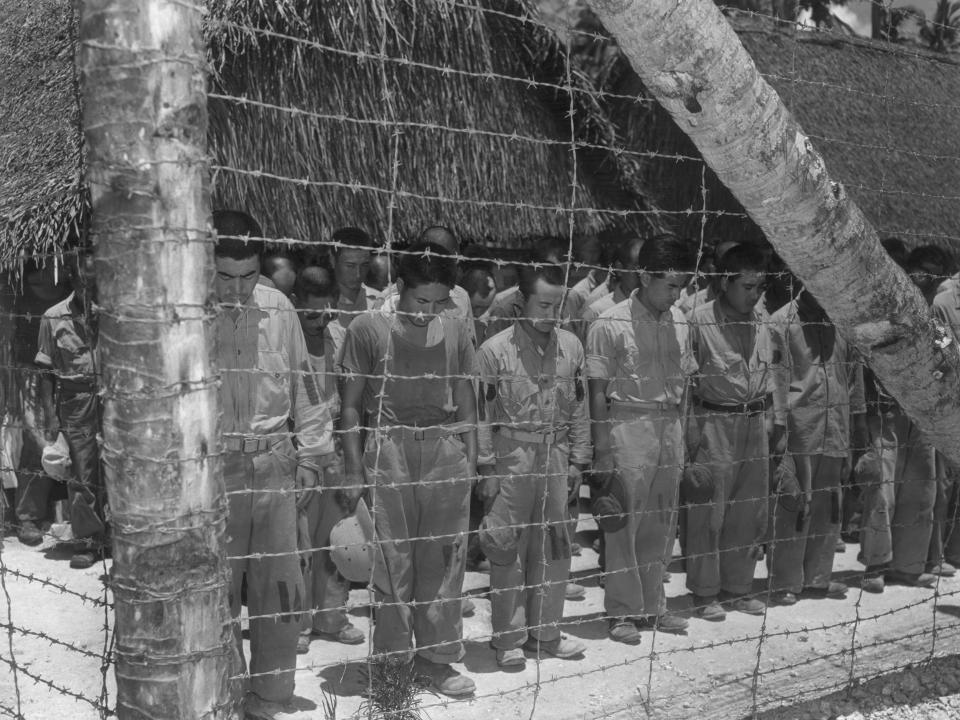 Japanese prisoners of war in Guam bow their heads after hearing Emperor Hirohito's announcement of Japan's unconditional surrender.