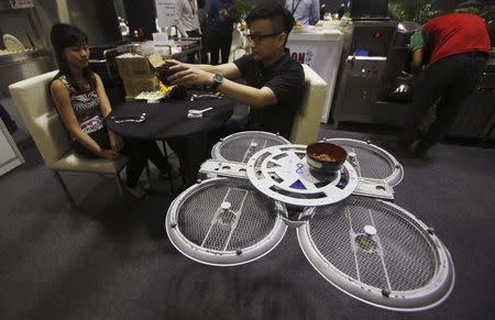 Visitors are served by an Infinium-Serve Unmanned Aerial Vehicle (UAV) that is designed to serve food and wait tables, at the National Productivity Month exhibition in Singapore, in this October 7, 2014 file photo. REUTERS/Edgar Su/Files