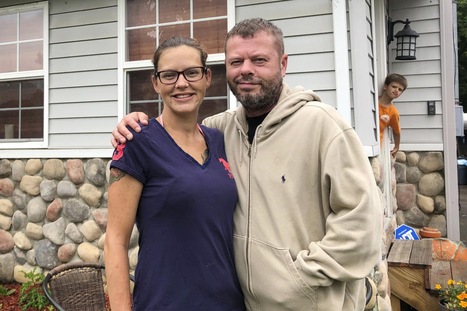 Crystal and Chris Martin stand outside their home, Sunday, July 19, 2020 in Burton, Mich., as one of their children looks on. The Martins, who had to defer some mortgage payments, are among millions of Americans who have struggled financially during the coronavirus pandemic. Crystal has been laid off since March from her job at a roller skating rink and Chris, an X-ray technician at a Flint hospital, was laid off, then took parental leave after the birth of a child this month. A new study by NORC at the University of Chicago finds that more than a quarter of Americans report losing income, investments and savings during the pandemic. (AP Photo/Tammy Webber)