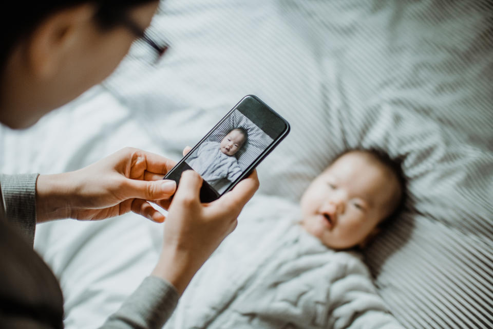 Mother photographing her baby girl with mobile phone on bed joyfully. (Getty Images)