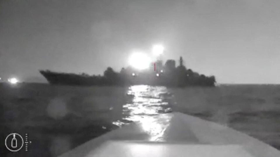 A blurry black-and-white screengrab from drone footage showing the silhouette of a ship.