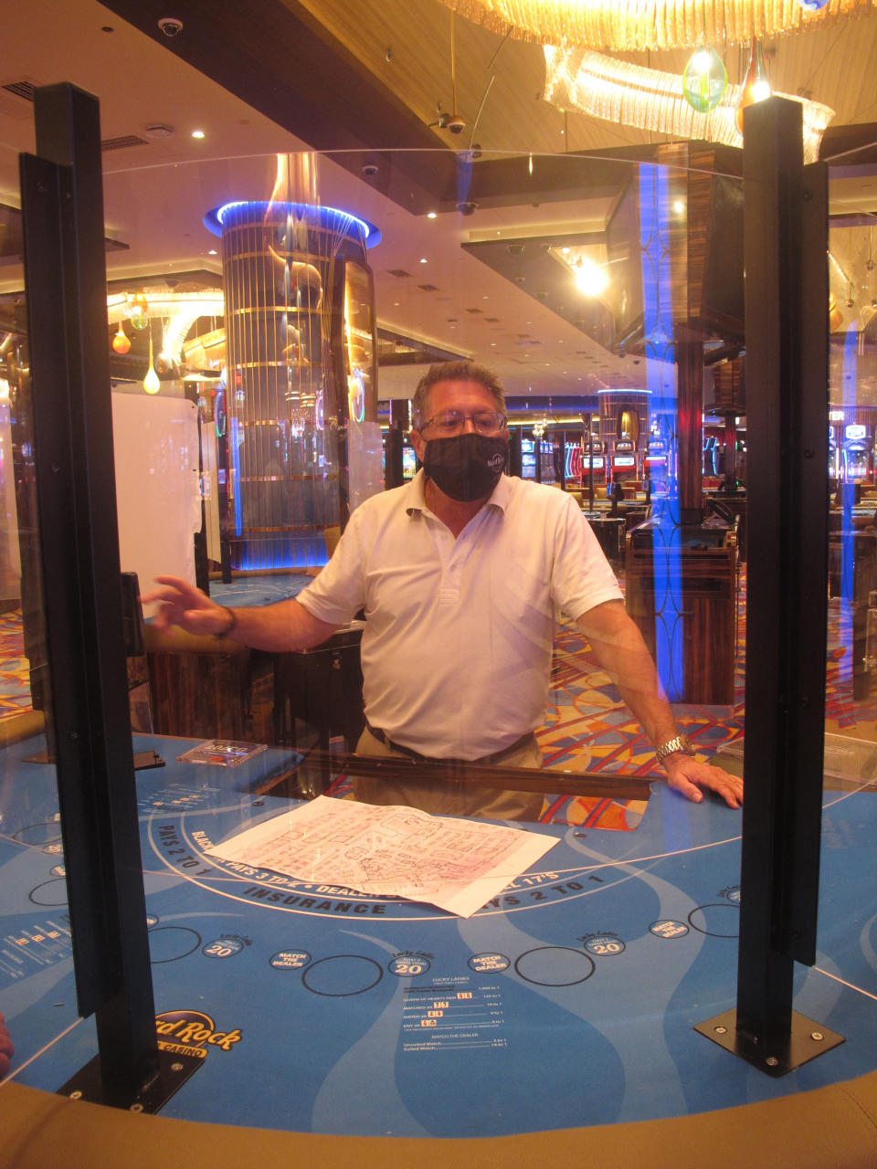 In this June 24, 2020 photo, Joe Lupo, president of the Hard Rock casino in Atlantic City N.J. examines the installation of protective barriers being installed at a card table on the casino floor. Smoking, drinking and eating will all be prohibited when Atlantic City's casinos reopen after being shut for three months due to the coronavirus outbreak under rules imposed by New Jersey Gov. Phil Murphy on June 29, 2020. (AP Photo/Wayne Parry)