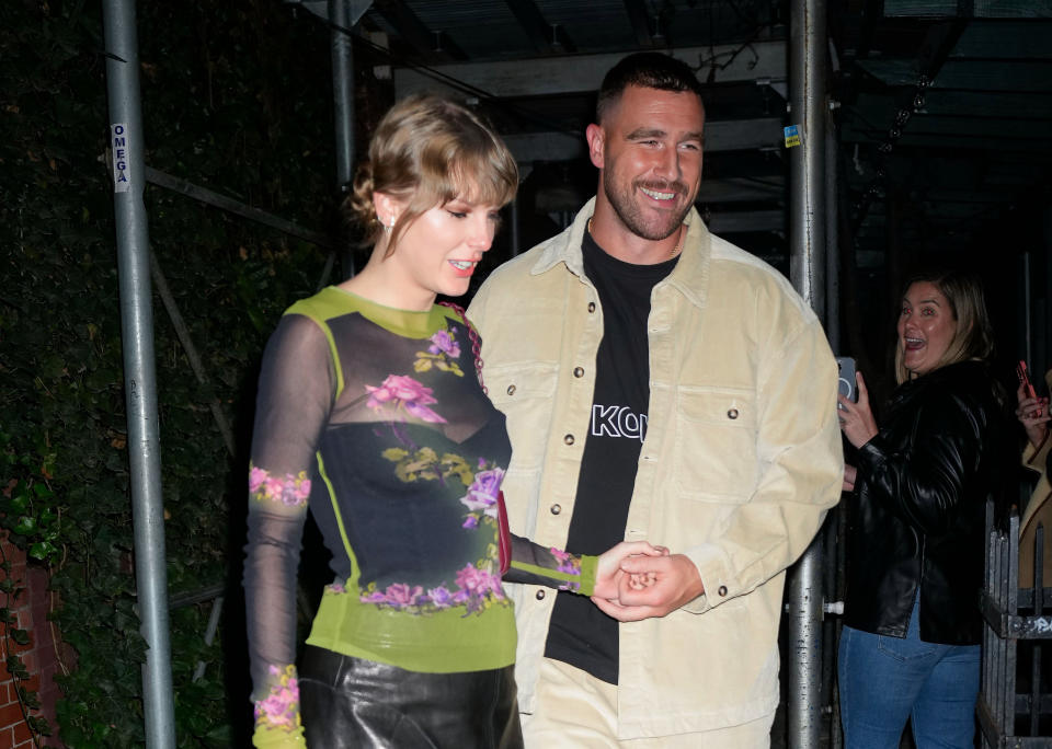 Taylor Swift in a floral outfit walking with Travis Kelce.